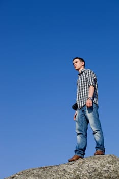 young casual man on top of a rock with the sky as background