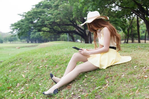 Woman sitting on grass and using a tablet. Located within the park.