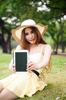 Women filed the tablet. Sitting on the grass in the park.