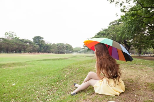 Woman with umbrella and sitting on the lawn. At the park