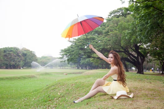 Woman with umbrella and sitting on the lawn. At the park