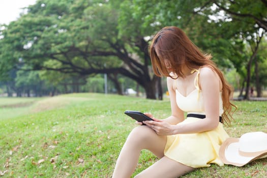 Woman sitting on grass and using a tablet. Located within the park.