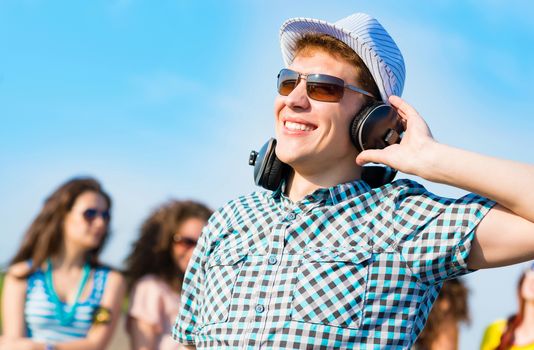 young man in sunglasses, headphones holds a hand on a background of blue sky and friends