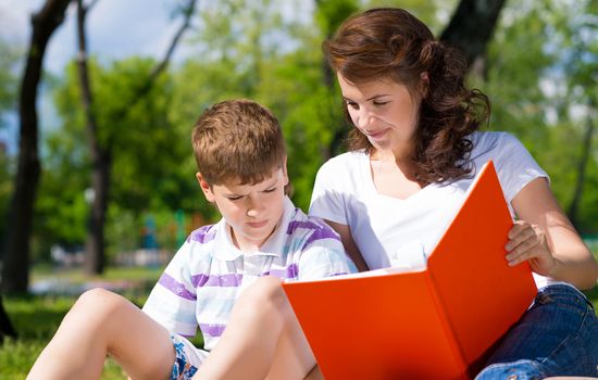 boy and a woman in a summer park reading a book together