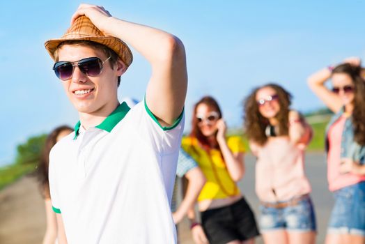 young man in sunglasses, a hat holds a hand on a background of blue sky and friends