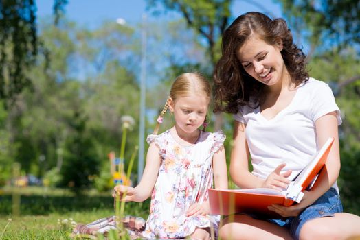 girl with the teacher reading a book together in the summer park