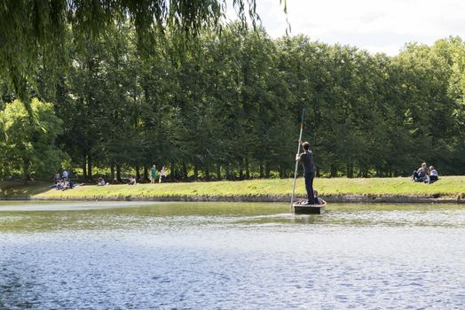 CAMBRIDGE, UK - AUGUST 18: Tourist punters in gondolas in River Cam with park full of trees in the background. August 18, 2013 in Cambridge.