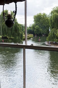 CAMBRIDGE, UK - AUGUST 18: River Cam with tourist punters in gondolas and park full of trees in the background viewed through old window with oil-lamp styled light. August 18, 2013 in Cambridge.