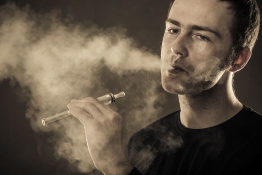 Man smokes electronic cigarette on dark background.