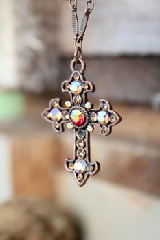Gem filled copper cross on necklace against wooden background