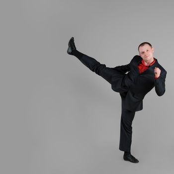 Businessman demonstrates a high kick on gray background