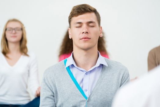 young man, meditating with closed eyes, group meditation