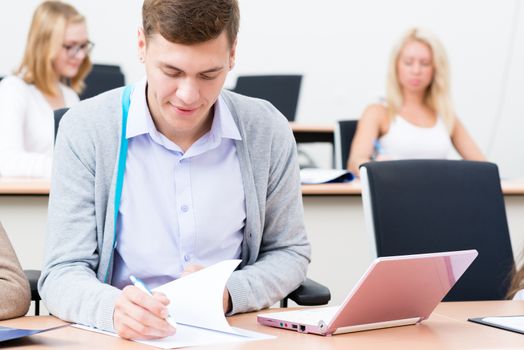 image of a student in the classroom keeps records, standing next to a laptop