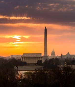 Bright orange sunlight illuminates clouds over Washington DC at dawn at sunrise. Lincoln, Washington Monument and Capitol are aligned