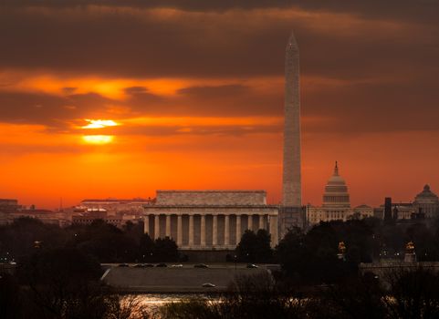 Bright orange sunlight illuminates clouds over Washington DC at dawn at sunrise. Lincoln, Washington Monument and Capitol are aligned