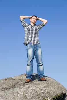 young casual man on top of a rock with the sky as background