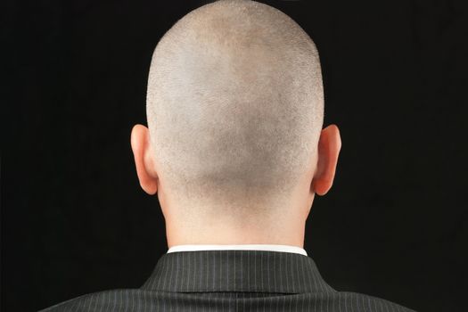 Close-up of a bald suited man, shot from behind.