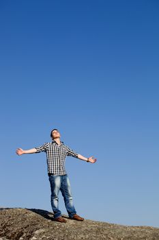 young casual man on top of a rock with the sky as background