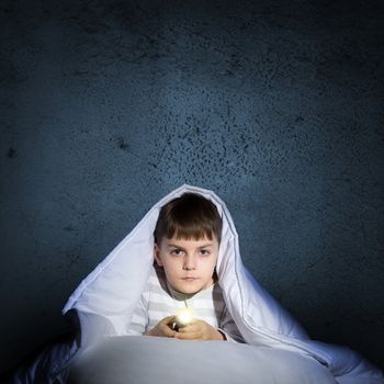 image of a frightened boy under the covers with a flashlight