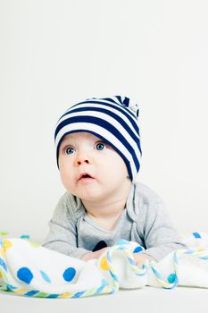 Portrait of a cute baby in striped hat lying down on a blanket