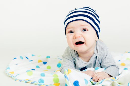 Portrait of a cute baby in striped hat lying down on a blanket