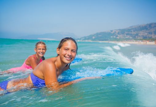 Summer vacation - Happy cute girls having fun with surfboard in the ocean