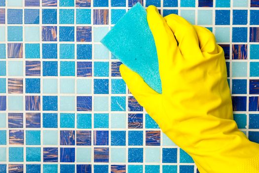 Hand in yellow protective glove cleaning mosaic wall with sponge