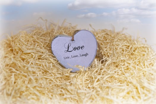 single wooden love heart in a love nest made of straw with light fluffy blue clouds