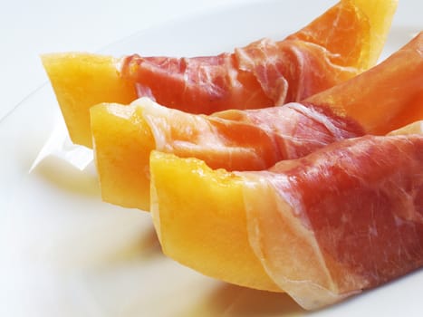 Summer breakfast or lunch background. Close-up of fresh and juicy ham and sliced yellow melon.