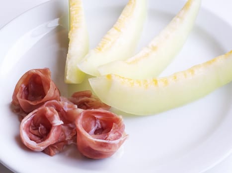 Summer breakfast or lunch background. Close-up of fresh and juicy ham and sliced yellow melon.