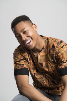 Portrait of handsome dark skinned male model smiling and wearing traditionally African clothes against white background