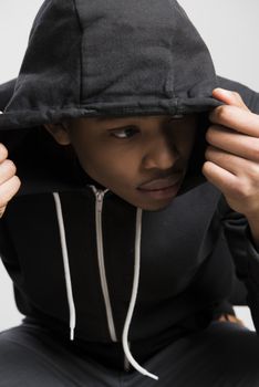 Portrait of suspicious dark skinned male model hiding under black hooded jumper