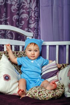 Little boy sitting in the nursery leaning on pillows on a cot