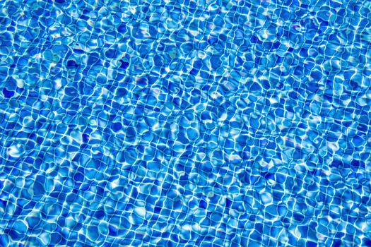 Abstract background of clear water in a dark blue tiled swimming pool.