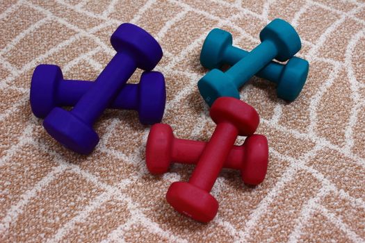 Blue, green, red dumbbells lie on the carpet ready for fitness classes