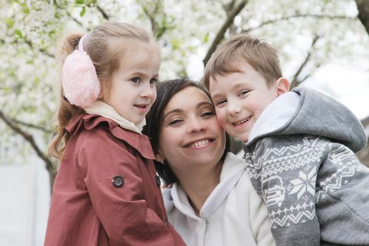 Happy mother and two children hugging among blooming garden