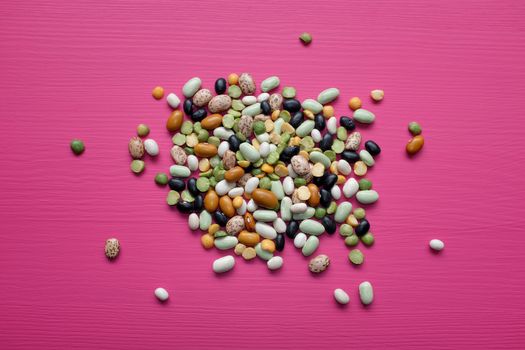 Mixed dried beans - black turtle beans, flageolet beans, pinto beans, brown beans, haricot beans, green split peas and yellow split peas - on a pink background