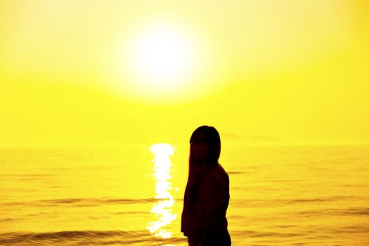 Young woman standing on beach under sunset light