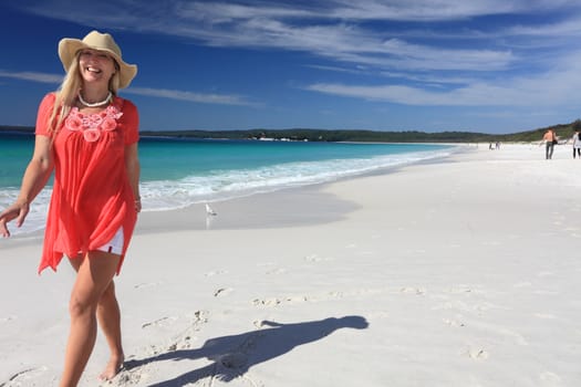 Happy vivacious smiling woman walking along the beautiful white sandy beach with pristine clear aqua waters and blue skies with  wispy clouds.    South Coast NSW Australia.    Space for message