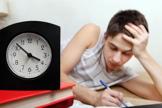 Teenager doing Homework in the Night at the Home. Focus on the Clock