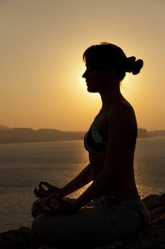 Young model is doing yoga on seaside at sunrise