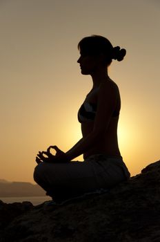 Young model is doing yoga on seaside at sunrise