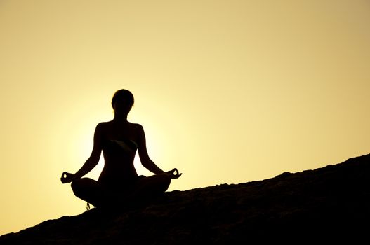 Young model is doing yoga on seaside at sunrise