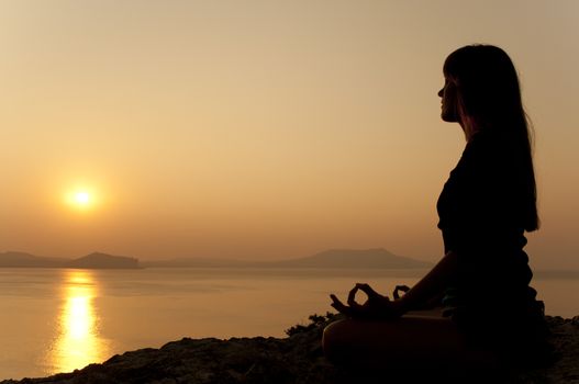 Young model is doing yoga on seaside at sunrise