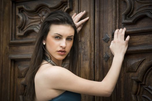 Pretty brunette girl outdoors with elegant dress leaning against old wood doors