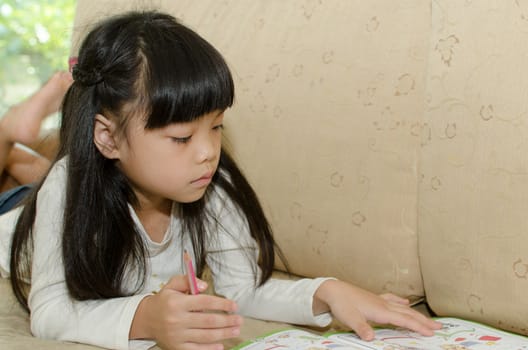 Cute little girl writing on a sofa.