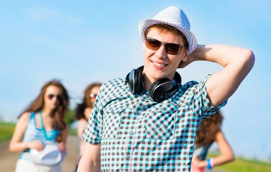 young man in sunglasses, a hat holds a hand on a background of blue sky and friends