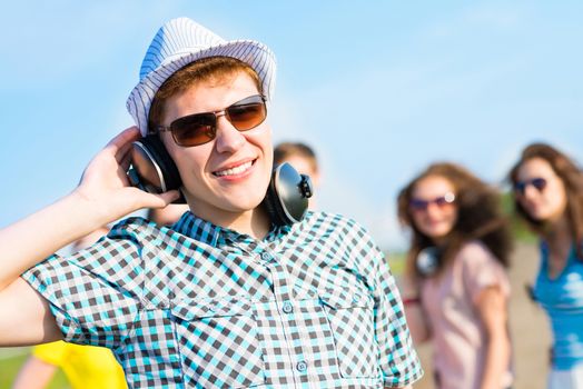 young man in sunglasses, headphones holds a hand on a background of blue sky and friends