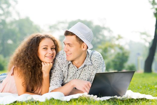 couple lying together in a park, working together on a laptop