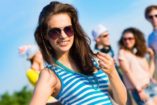 stylish young woman in sunglasses on the background of blue sky and friends